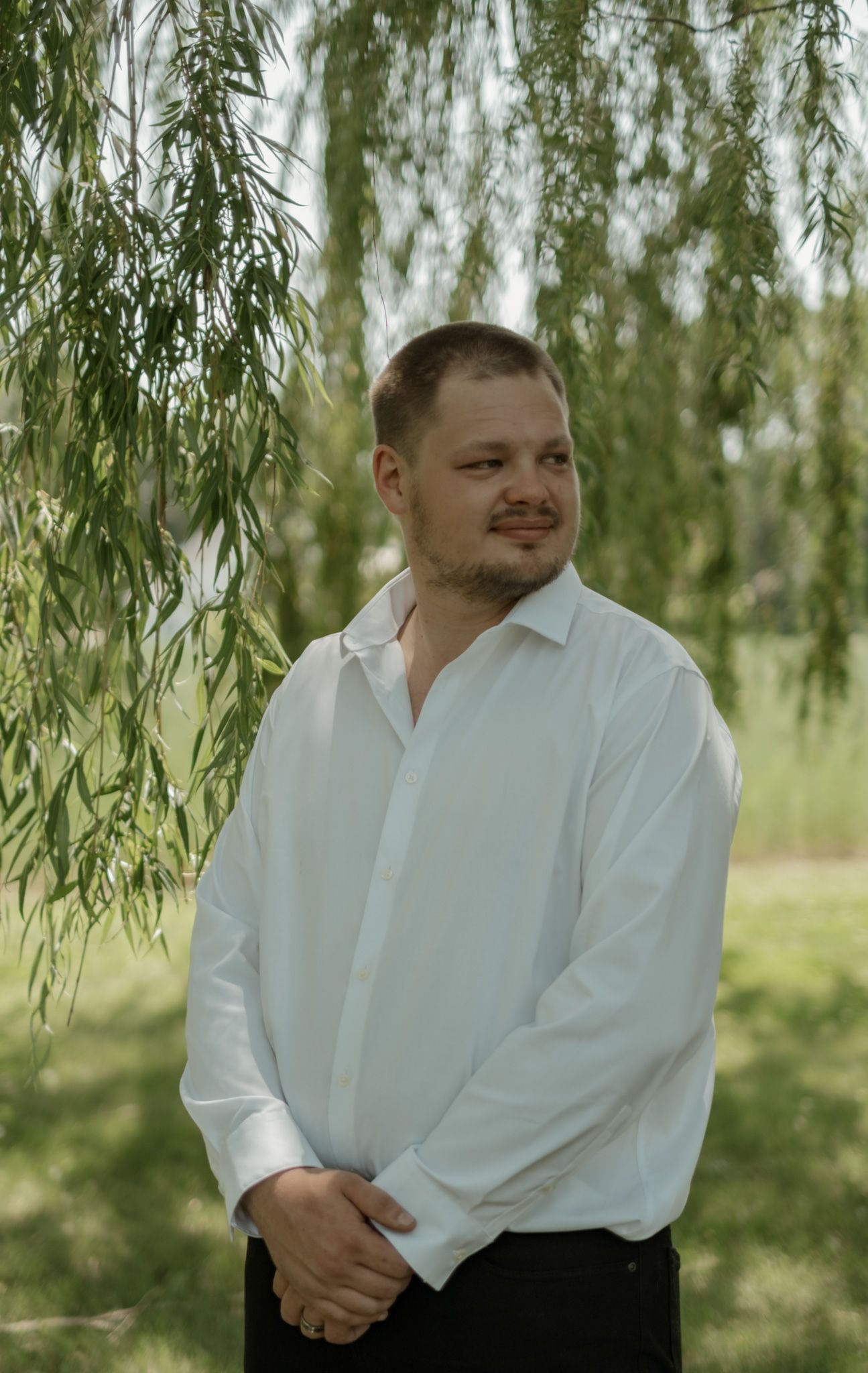 Someone in a white shirt stands under a willow tree in a natural outdoor setting.