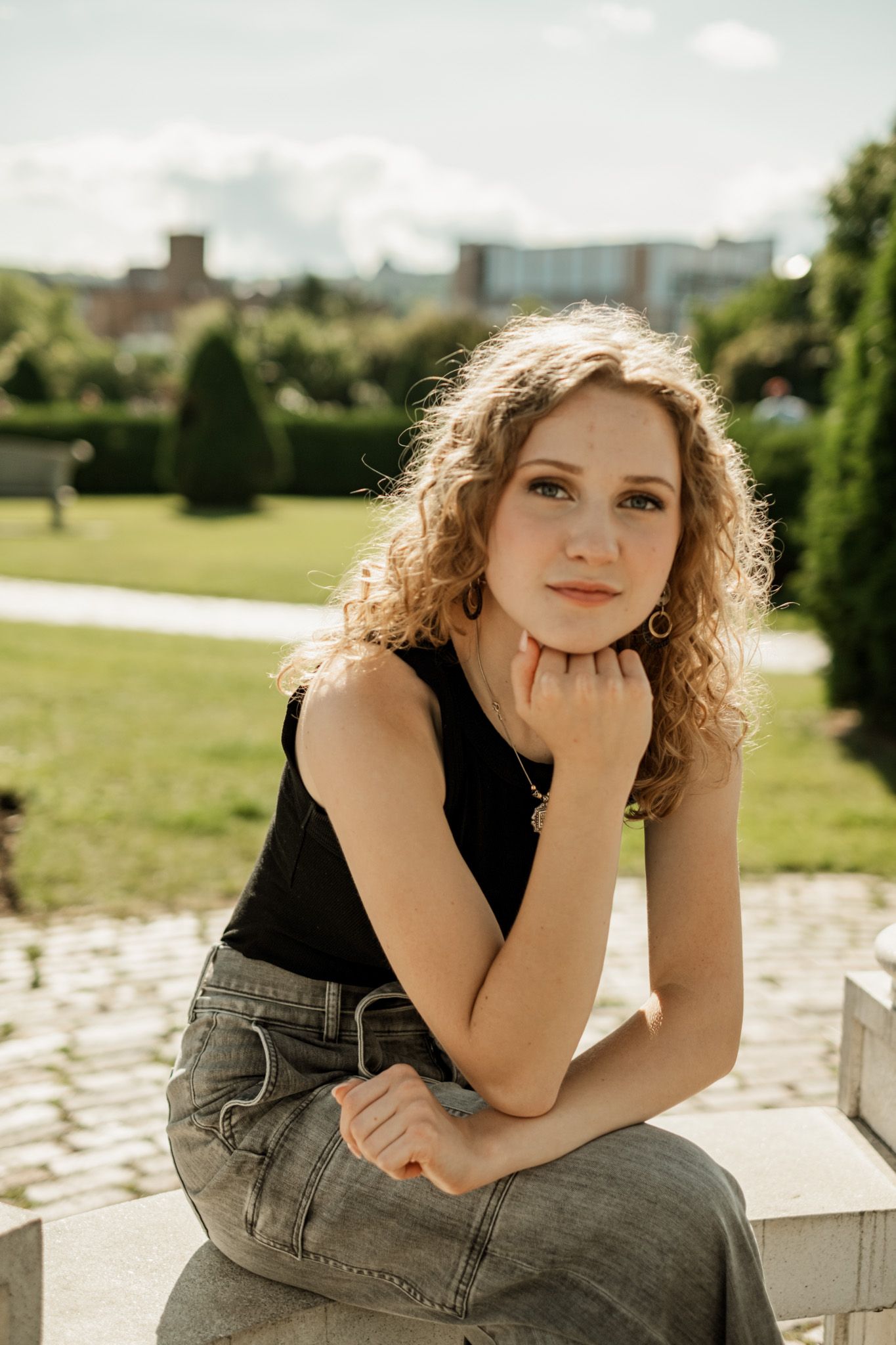 Casual outdoor portrait series showing a person in a black top and denim jeans sitting on concrete steps in sunlight.