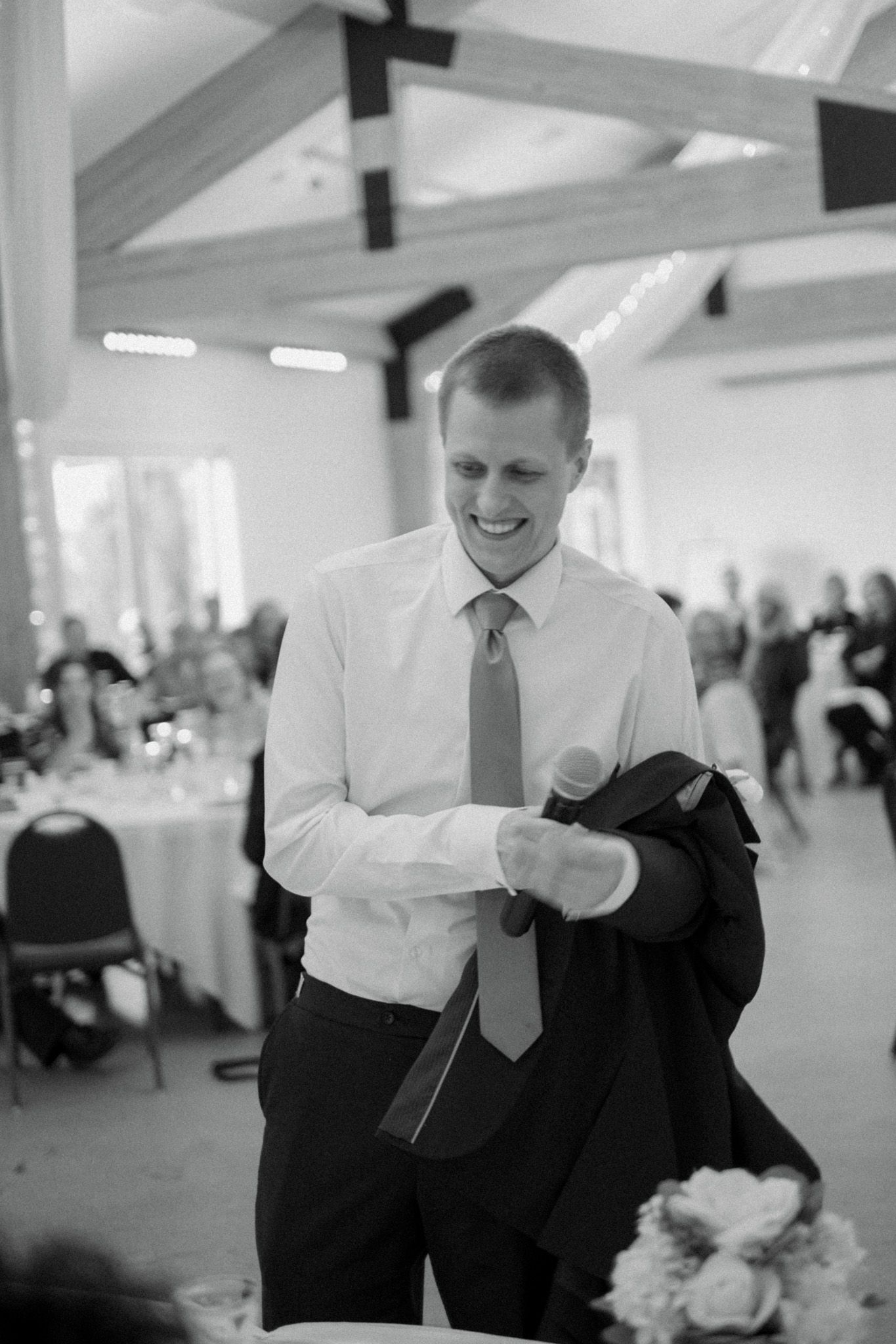 A candid black and white photo shows a guest smiling while holding a jacket at a formal event.