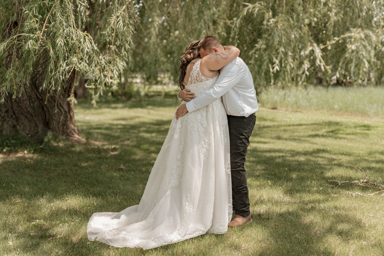 A couple embraces under a willow tree during their outdoor garden wedding ceremony.