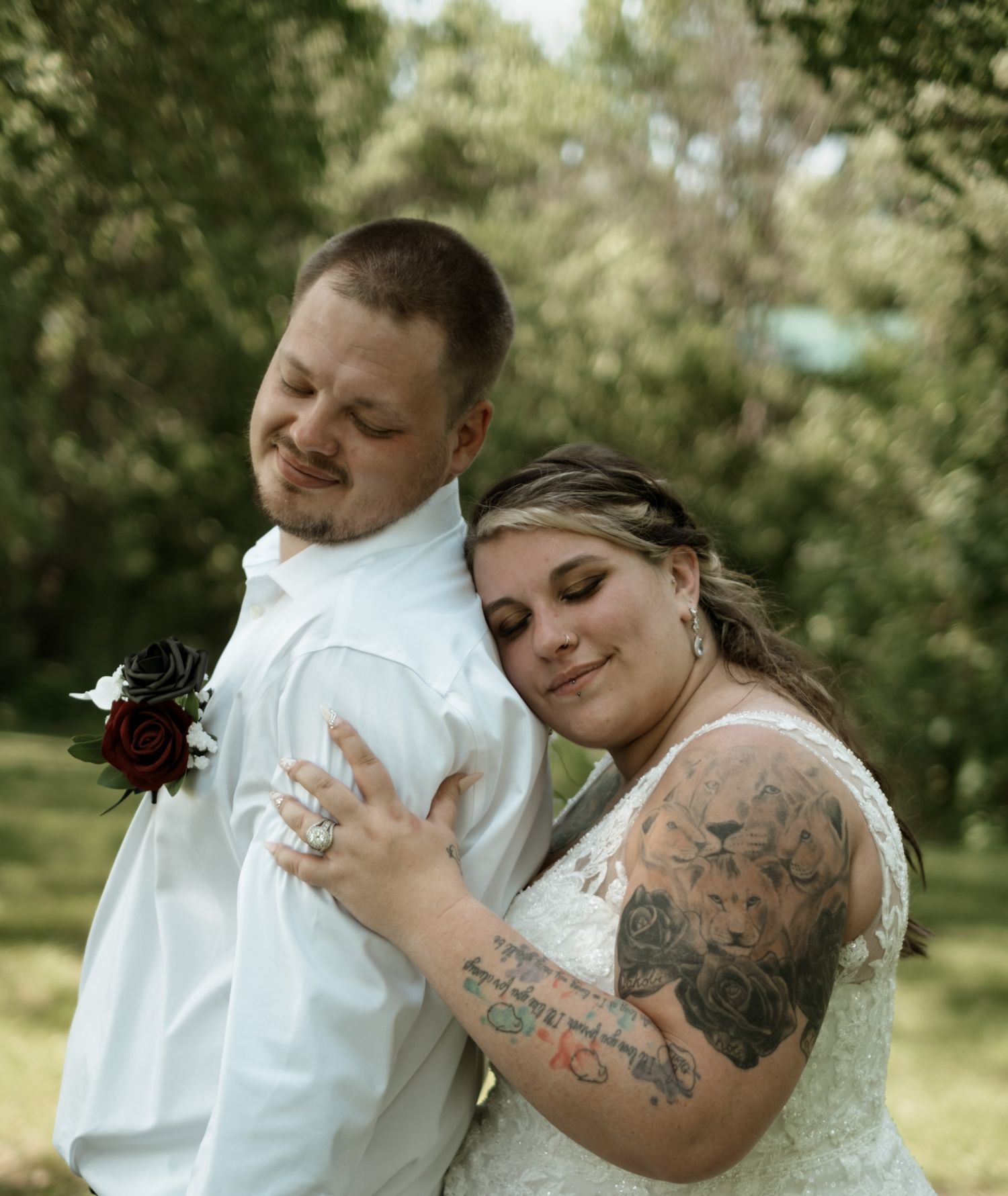 A couple dances gracefully in an outdoor garden setting, with the person in white dress showing visible tattoo artwork.