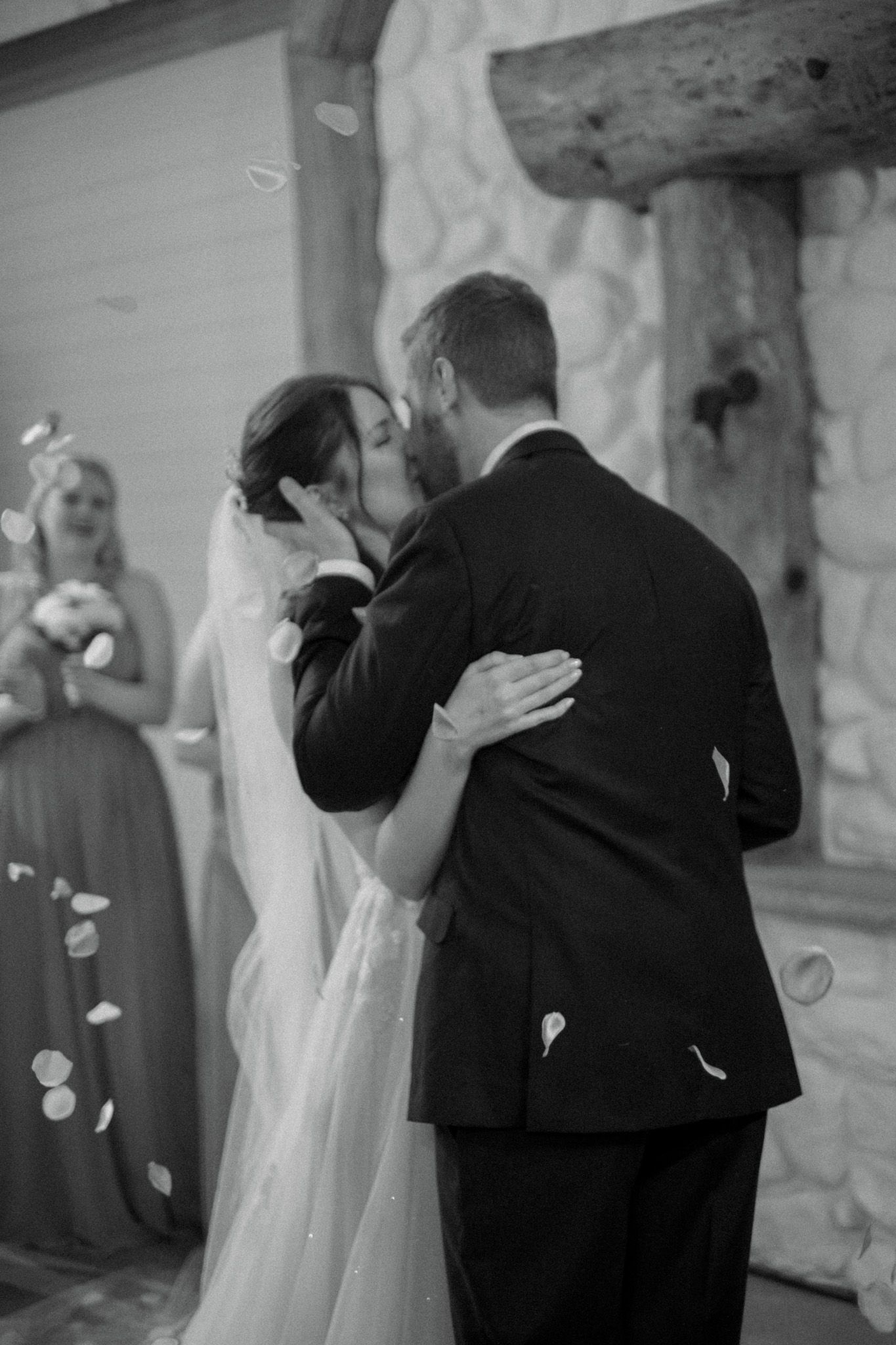 A romantic black and white photo of newlyweds sharing their first kiss at their wedding ceremony.