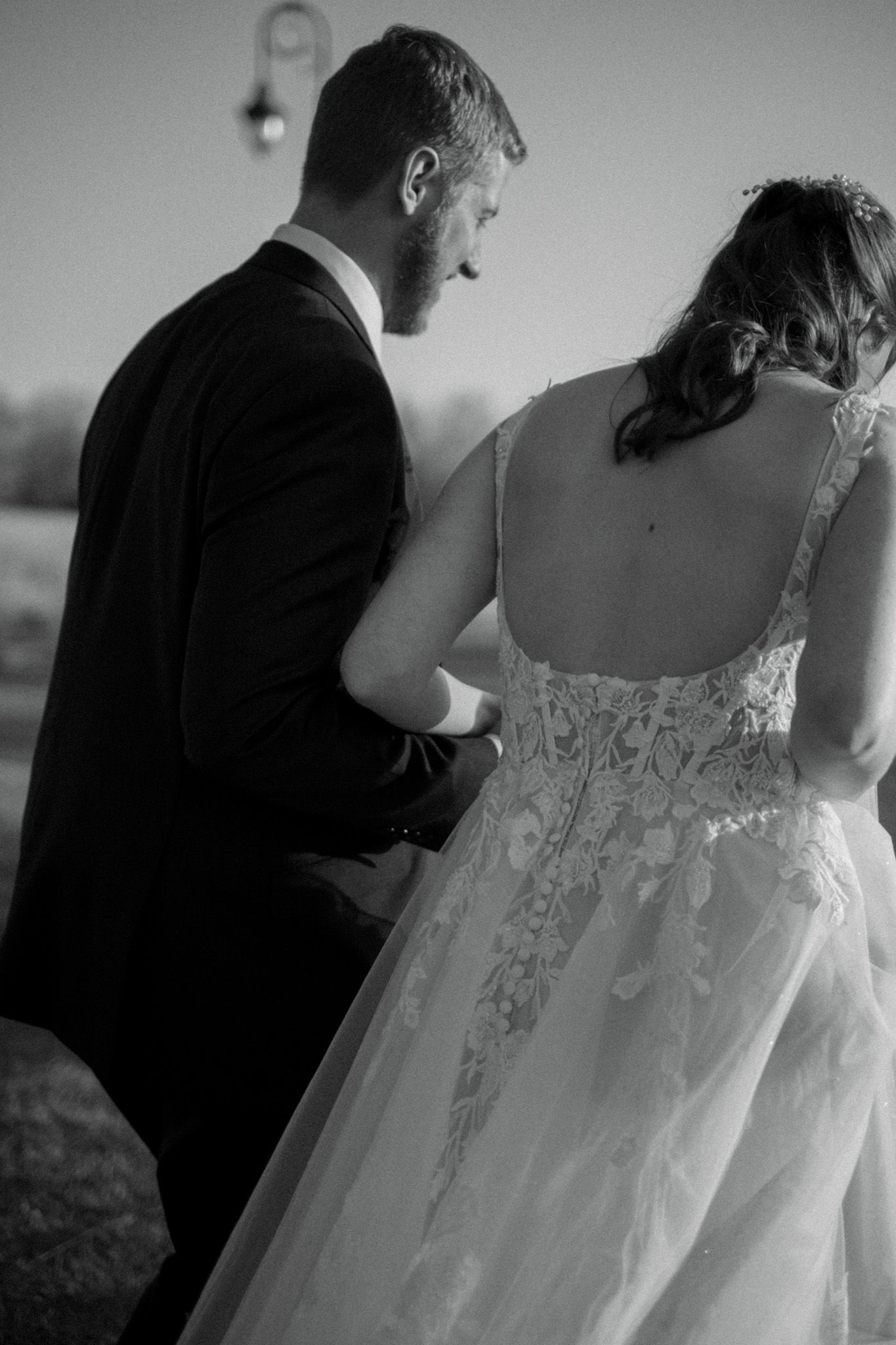 A black and white portrait of a couple showcasing the intricate lace details of the bride's dress.