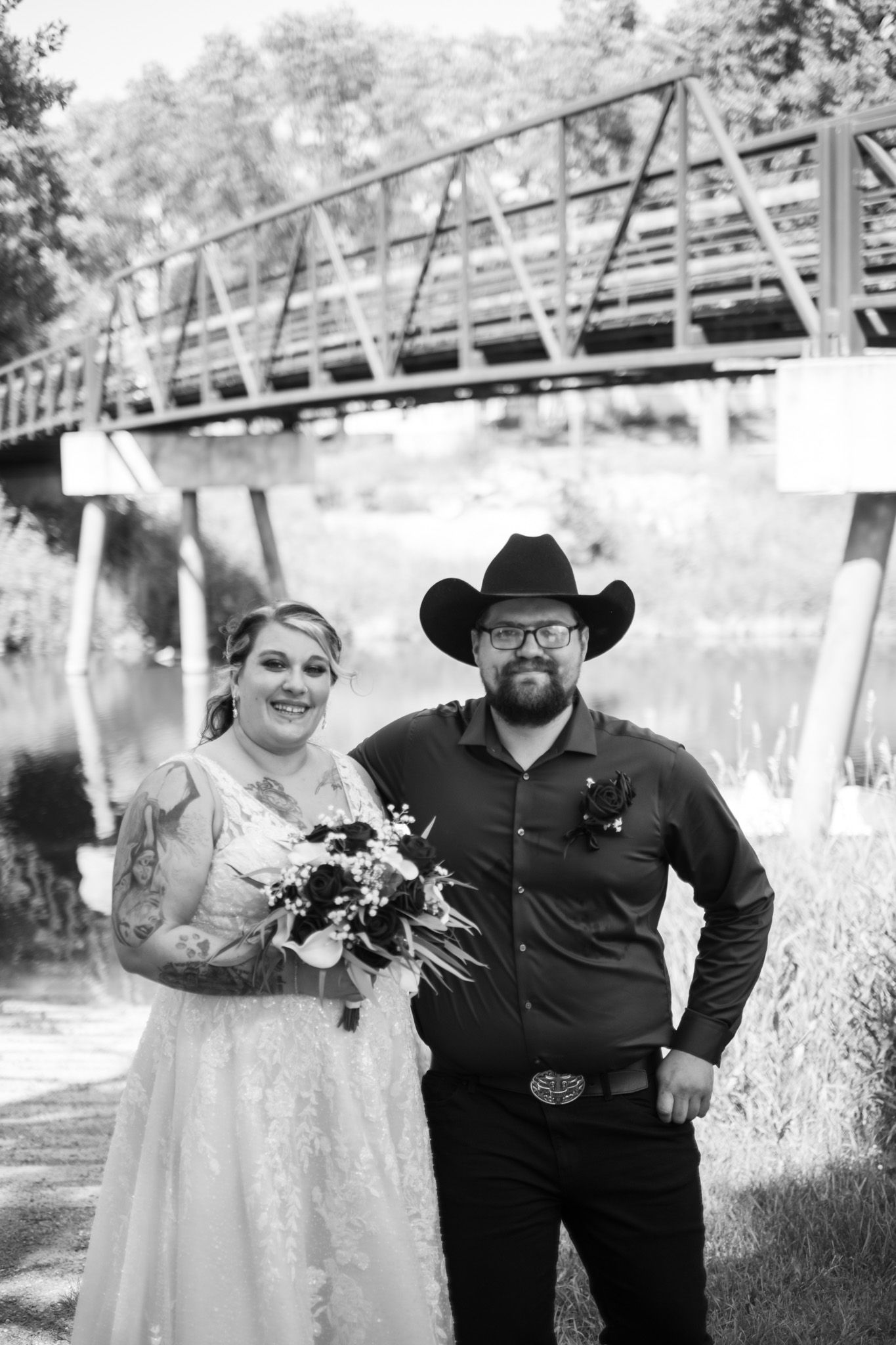 Black and white wedding portraits showing a couple posing outdoors near a rustic bridge.