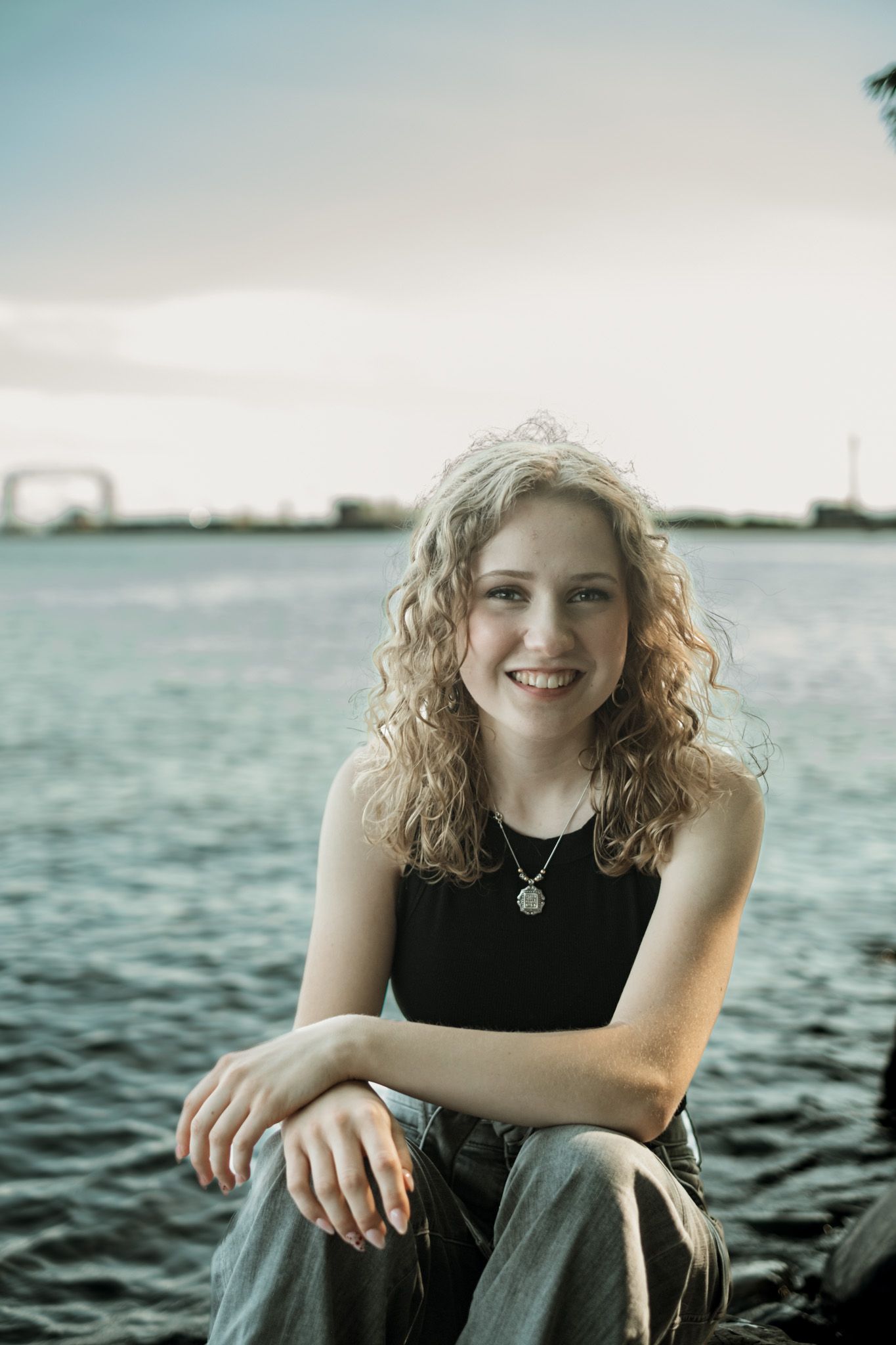 Four waterfront portrait shots featuring a person with curly hair wearing black against a serene water backdrop at sunset.