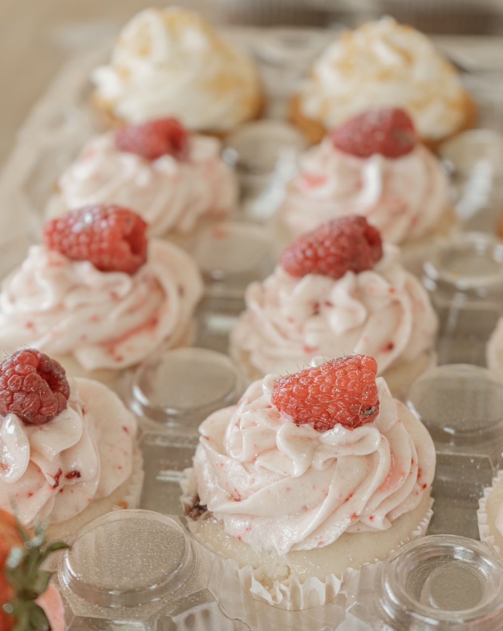 Pink frosted cupcakes topped with fresh raspberries arranged on clear glass plates.