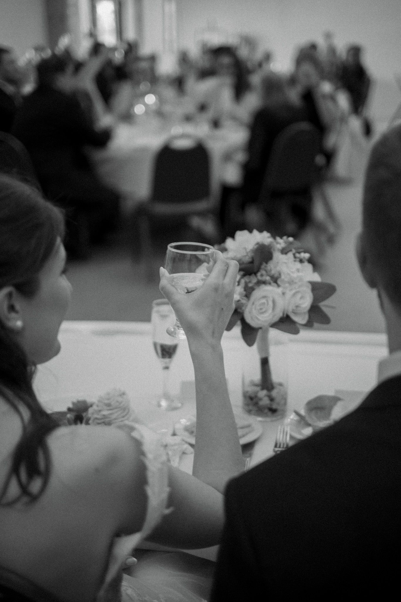 A black and white photo captures guests at a wedding reception raising glasses for a toast.