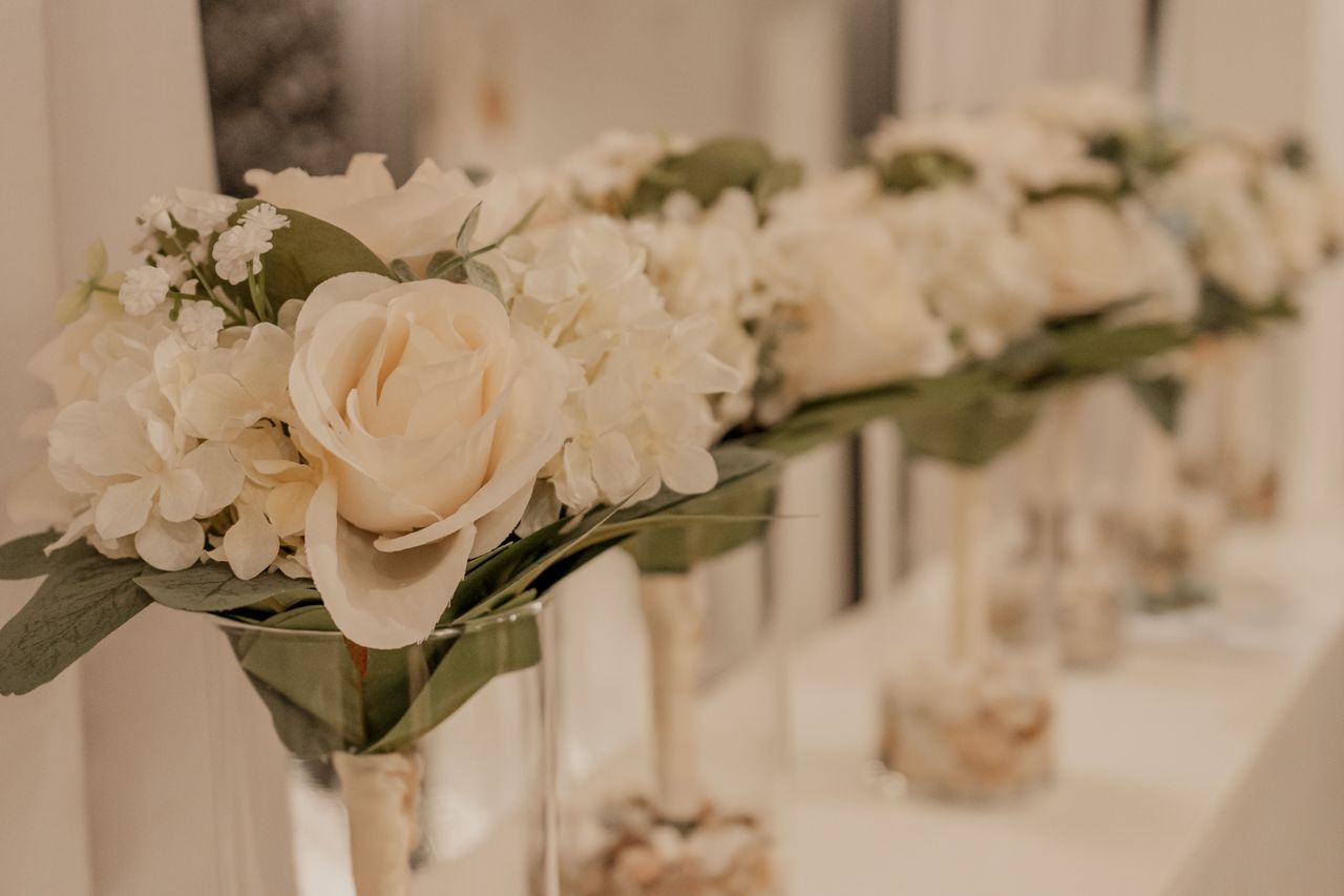 Elegant white rose and hydrangea flower arrangements in vases lined up for wedding decoration.