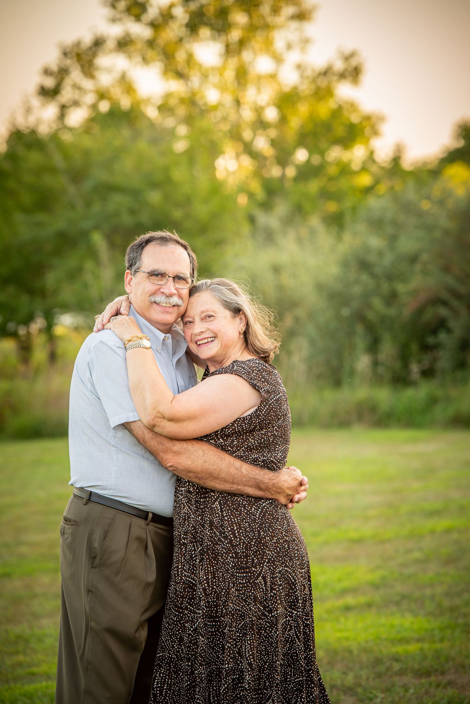 Chalco Lake Family Photography - A couple embraces lovingly in a garden setting at sunset as golden light filters through trees.