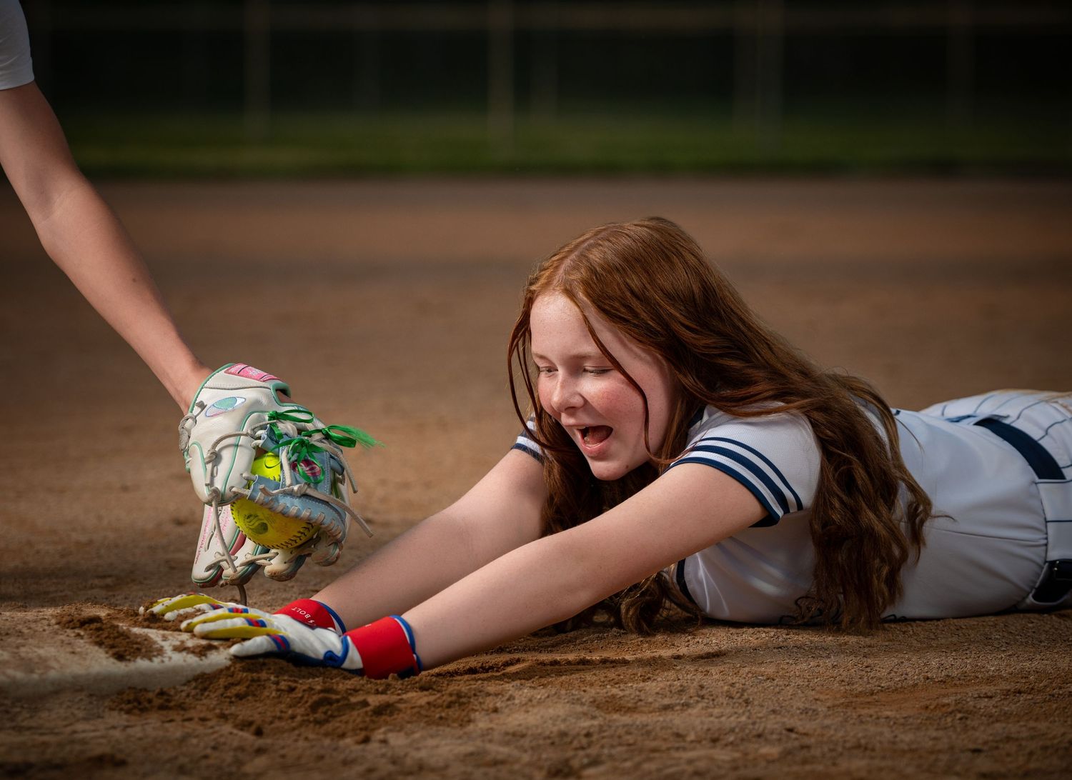 Softball player slides into base on dirt field with outstretched glove during competitive game taken by Omaha sports photographer.
