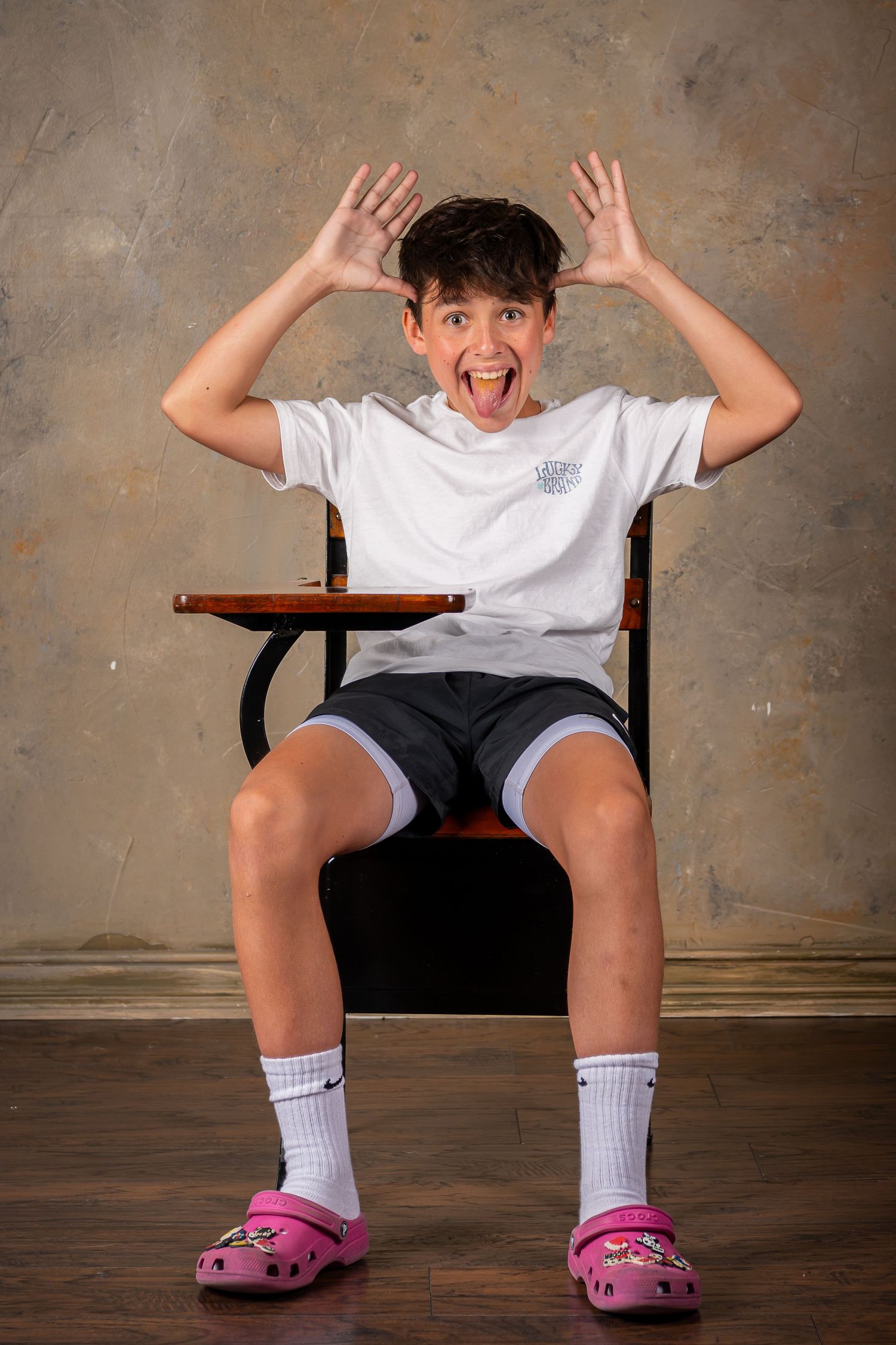 A student seated, wearing a white t-shirt, black shorts and pink crocs shoes during a children's photography session in Omaha.
