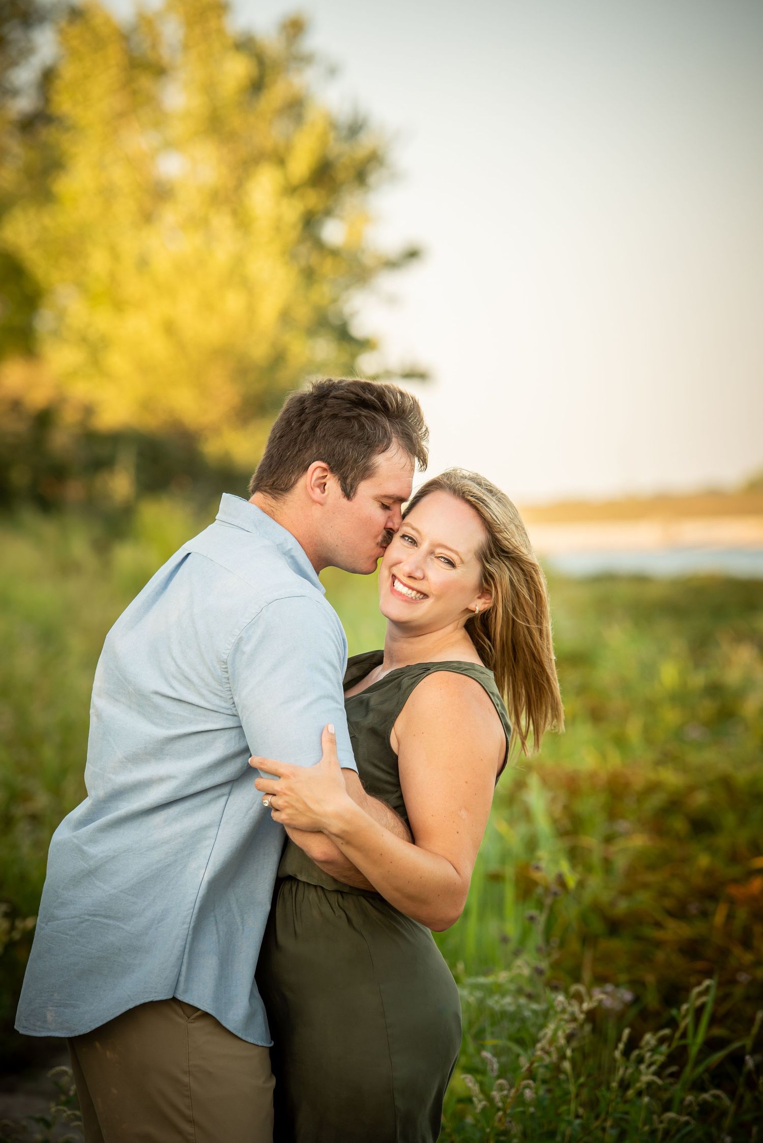 Chalco Lake Family Photo - A romantic couple embraces in a field during golden hour, with autumn trees, sunlight creating a warm atmosphere.