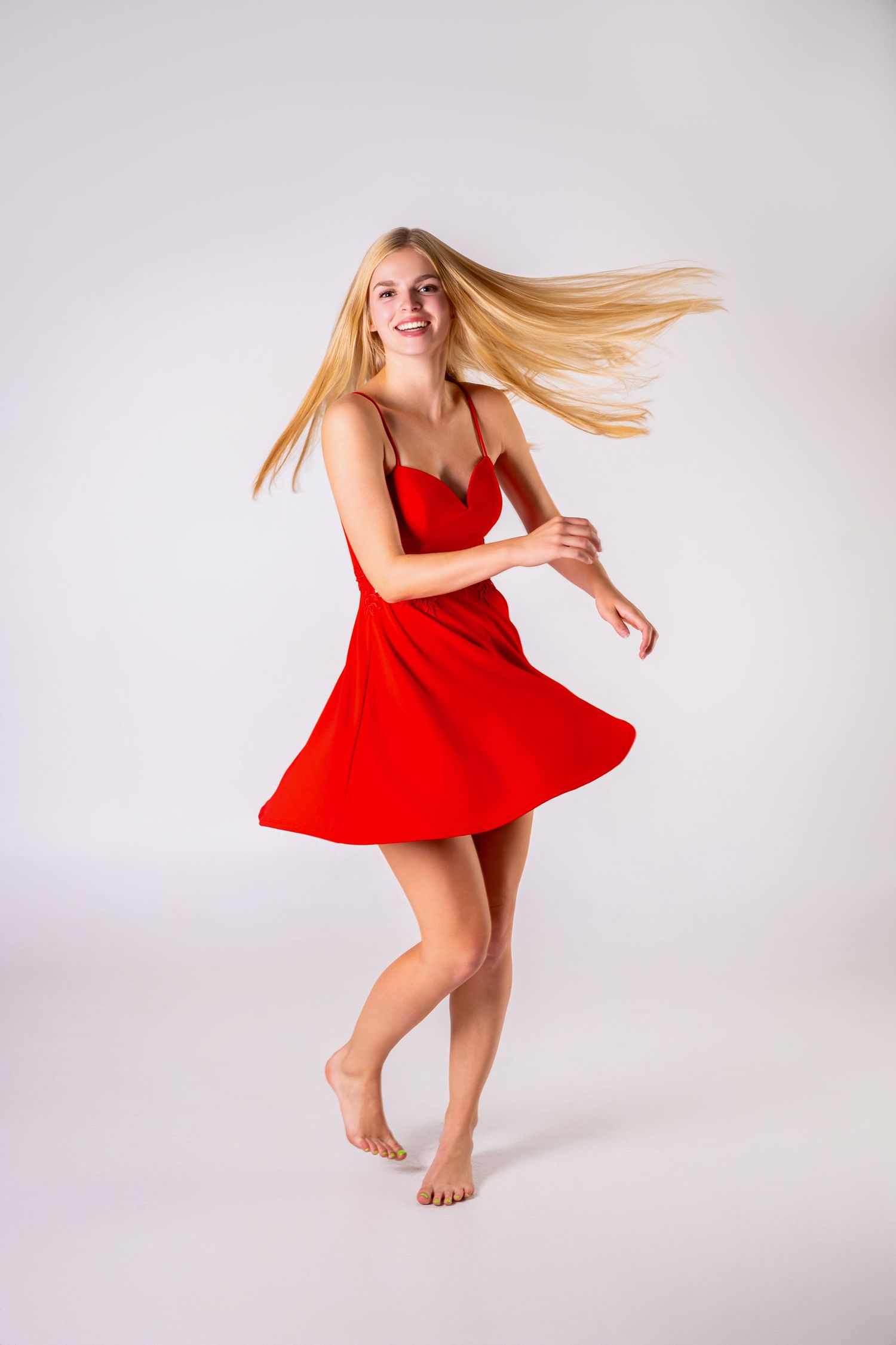 Omaha Senior Photography - Photographer in Omaha - Woman in red sundress dances barefoot with flowing hair against white backdrop.