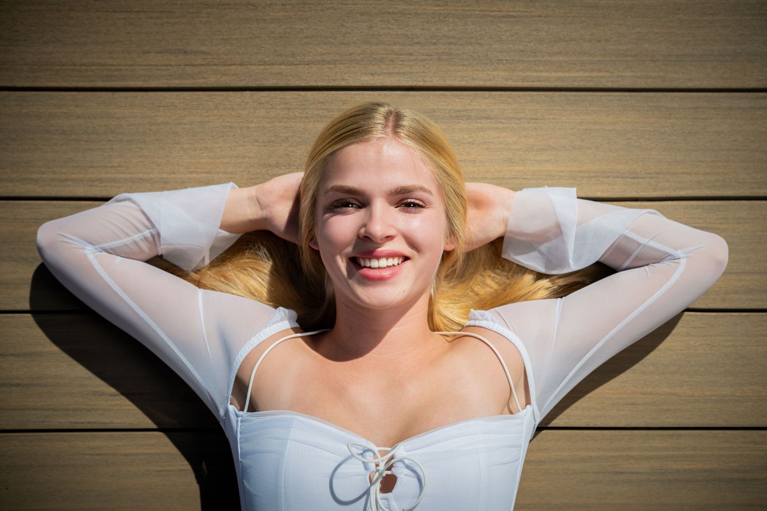 Omaha Senior Photography - Photographer in Omaha - Woman relaxing on wooden deck in white top with sunlit blonde hair.