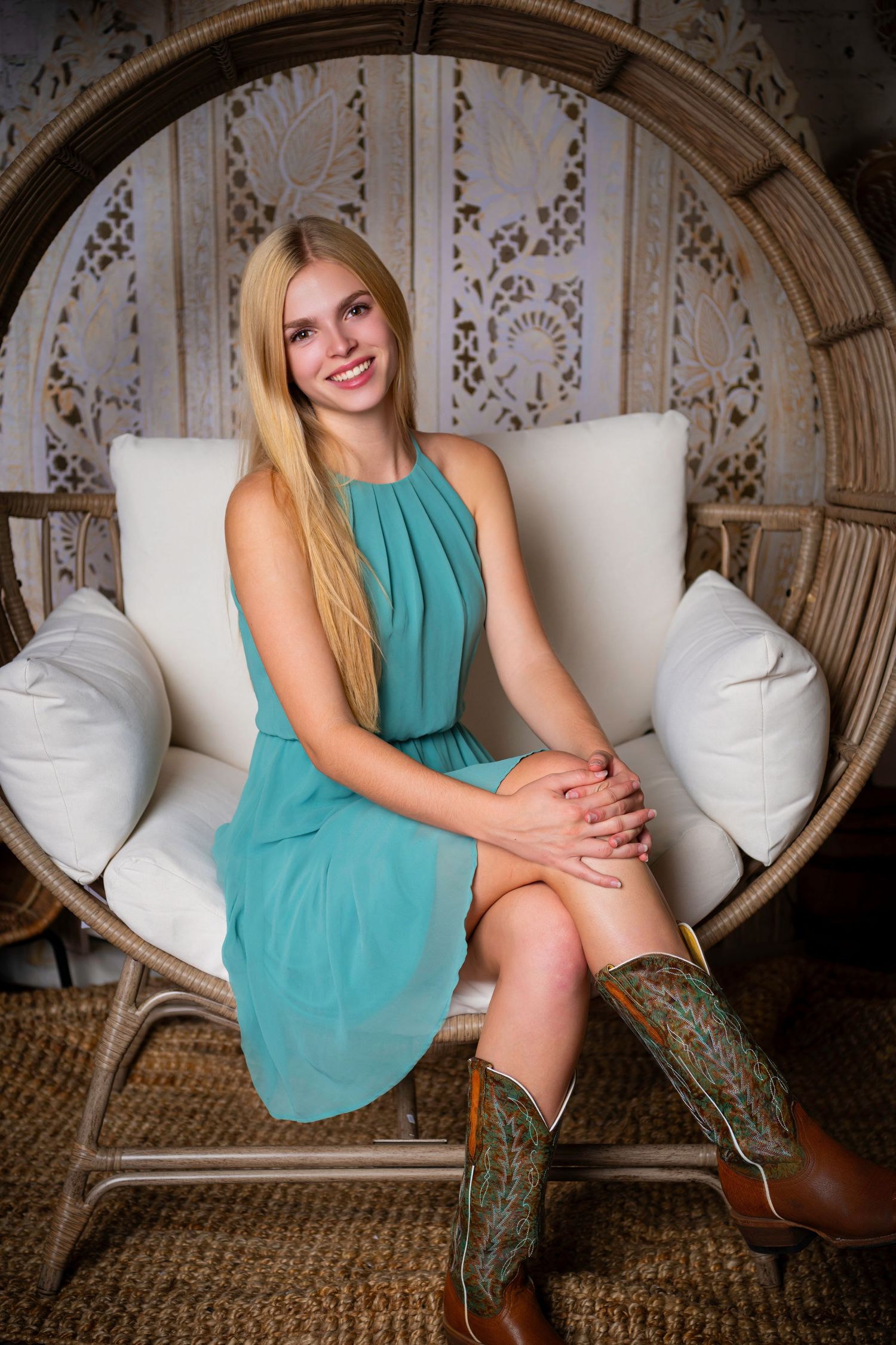 Omaha Senior Photography - Photographer in Omaha - Woman in teal dress sits in wicker egg chair wearing western boots.