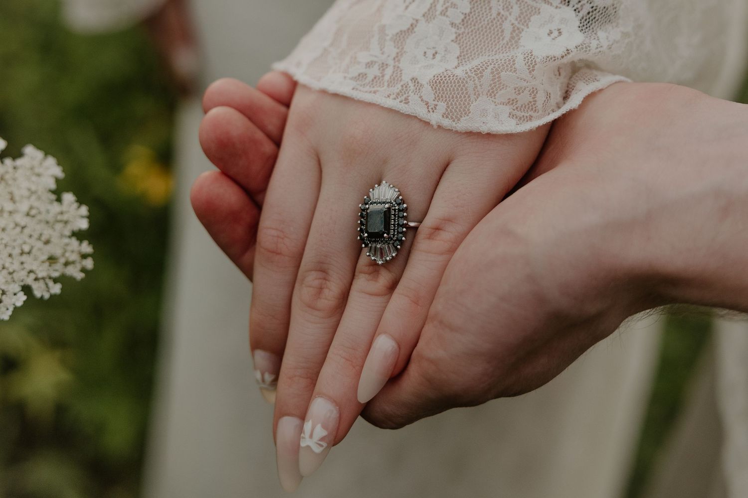 Close-up of hands displaying an ornate vintage-style ring against lace dress fabric.