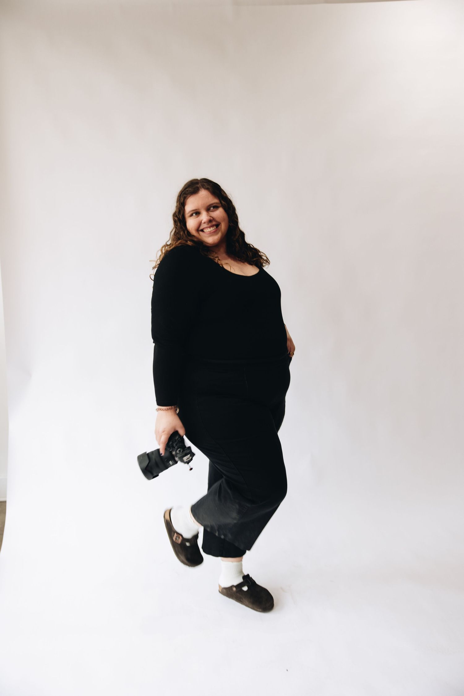 Creative studio portrait of photographer holding camera while posing playfully against white background.