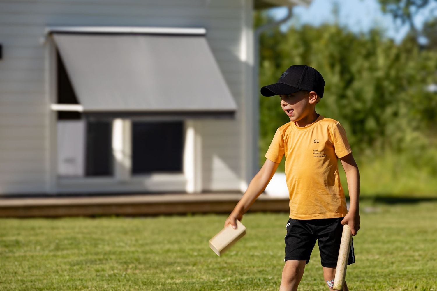 En ung person i en gul t-shirt spelar ett kubb en solig sommardag.
