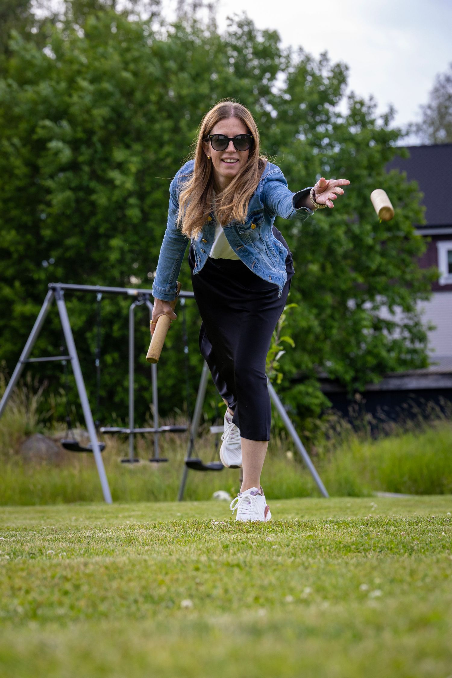 Kvinna i jeansjacka spelar kubb på gräsmattan.