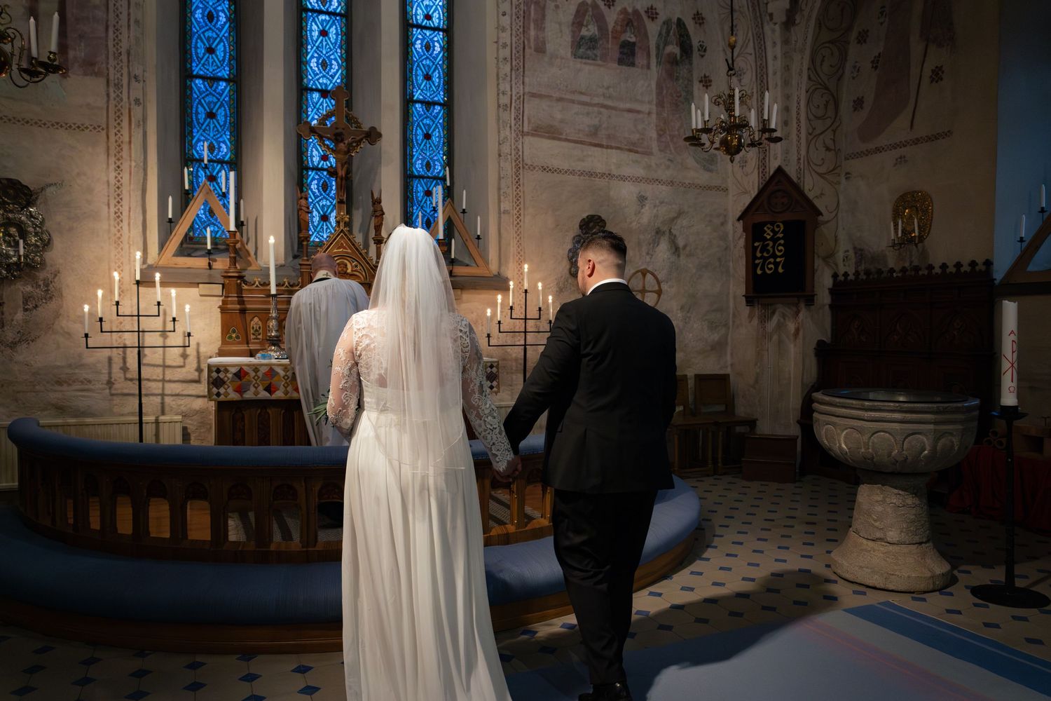 Ett par står vid altaret i en kyrka med glödande blå glasmålningar under sin vigselceremoni.