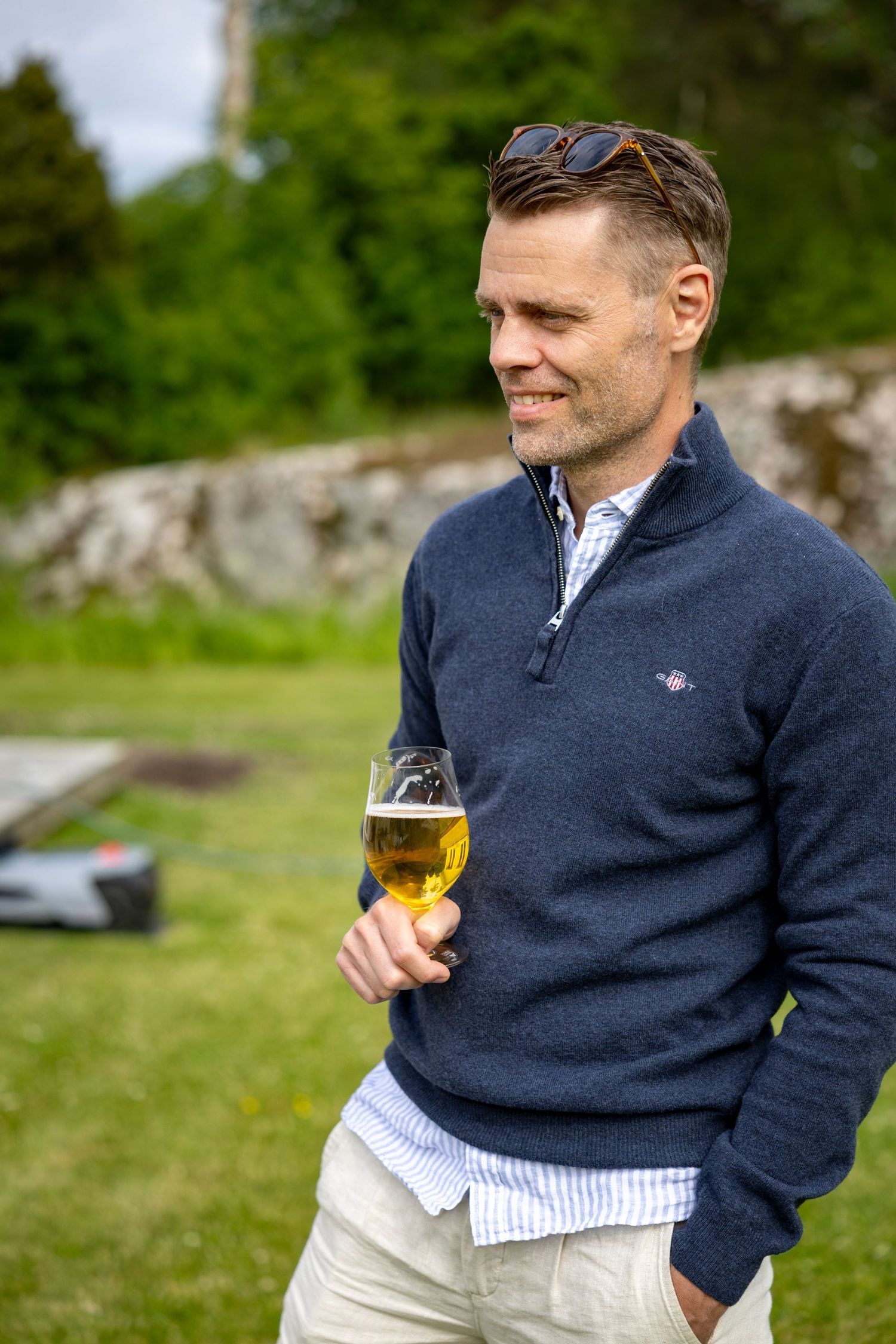 En person i en marinblå tröja som håller ett ölglas utomhus en molnig dag.