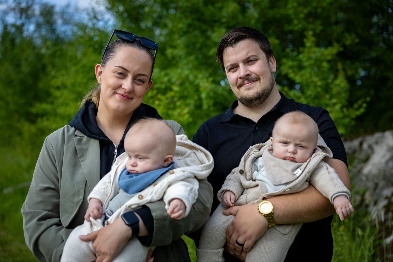Familjeporträtt med tvillingar i matchande vita kläder mot grönt bladverk.