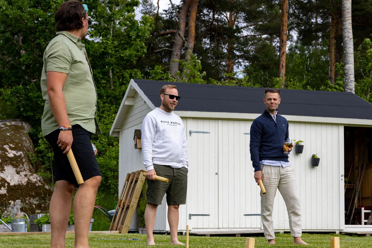 Tre personer står och pratar under kubb spel på en bakgård.
