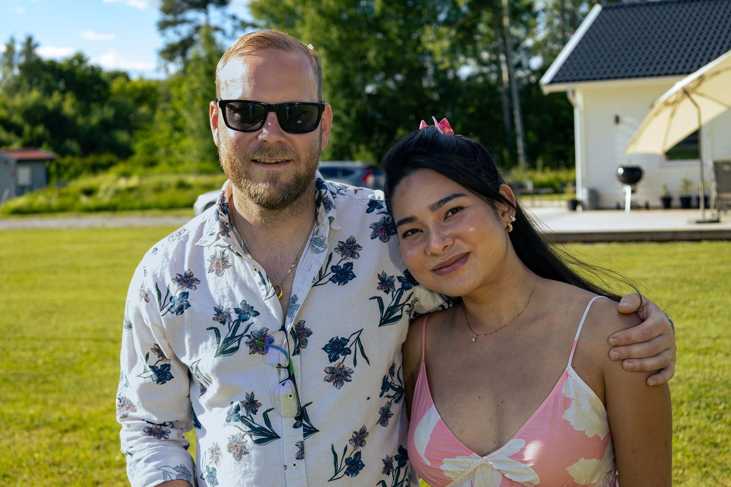 Två personer i sommarkläder poserar tillsammans på en solig gräsmatta.