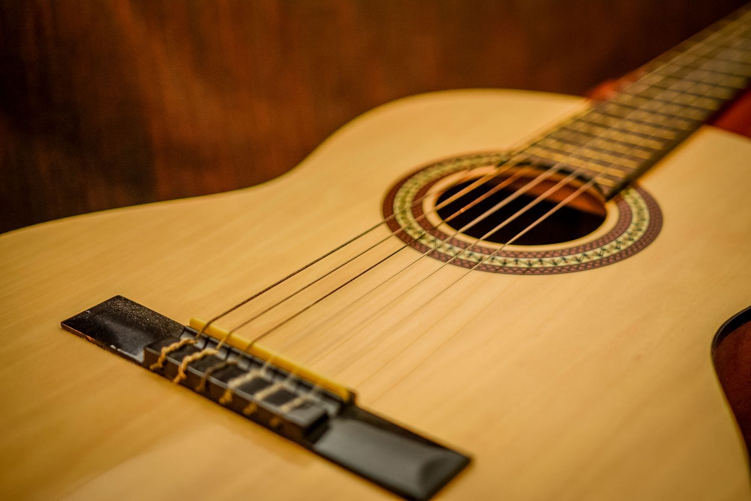 Close-up view of a natural wood acoustic guitar showing the bridge, strings, and decorative rosette detail around the soundhole.