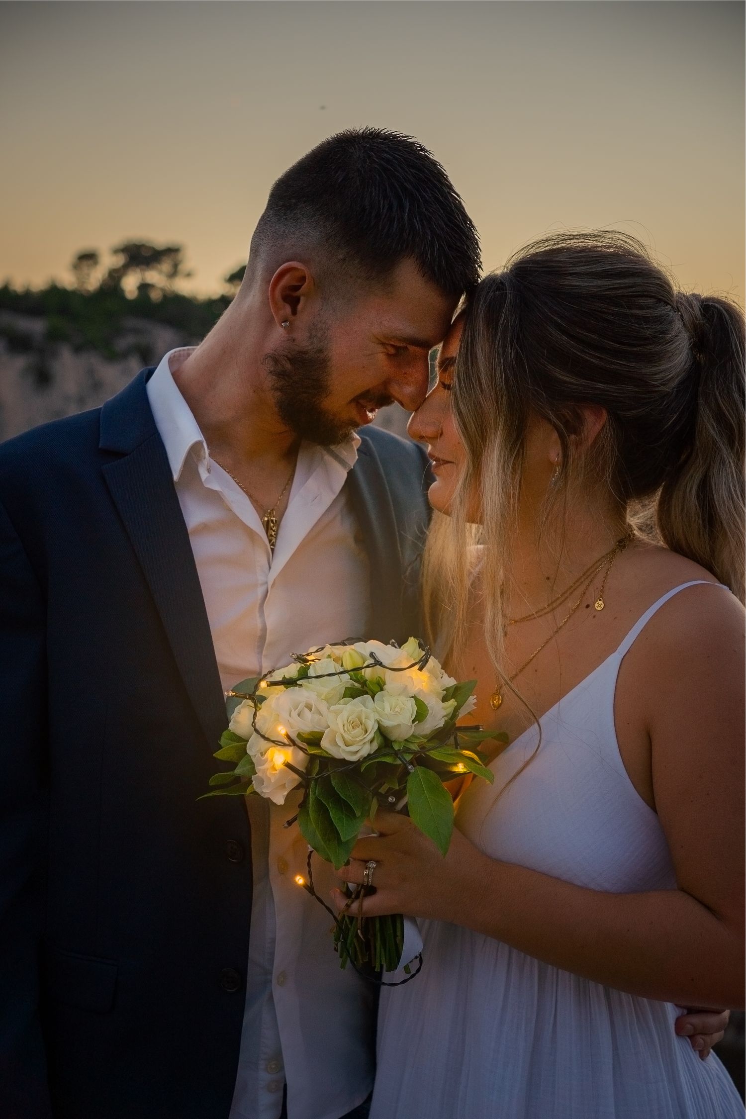 A romantic sunset wedding photo shows a couple in white and black sharing an intimate moment while holding a rose bouquet.