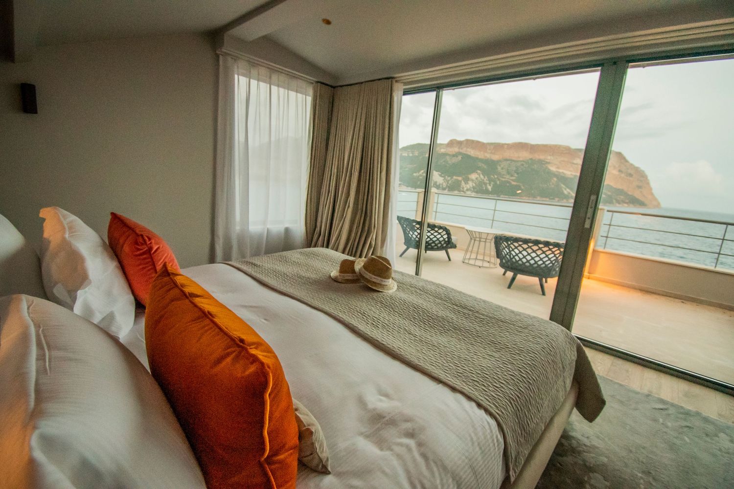 Luxurious hotel room with orange accent pillows and a private balcony overlooking scenic ocean views.