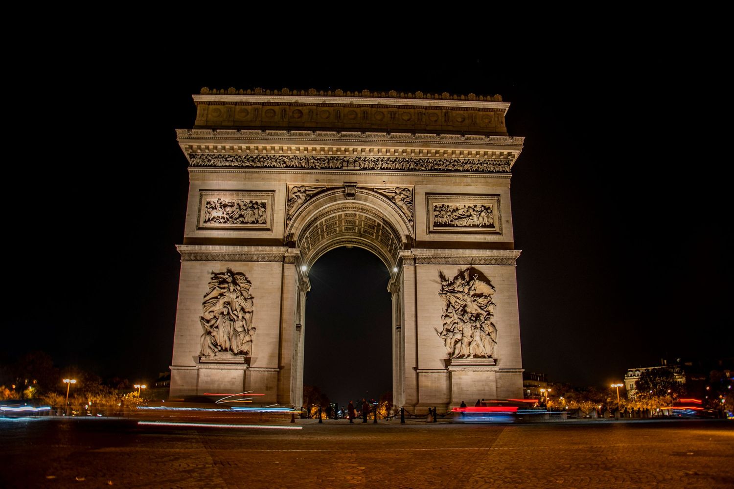 The Arc de Triomphe in Paris illuminated at night against a dark sky with light trails from passing traffic.