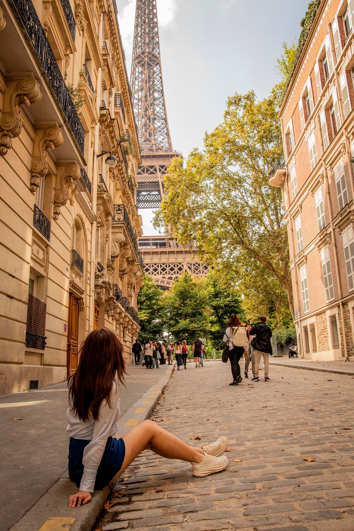 View of the Eiffel Tower from a charming cobblestone street in Paris with classic buildings and trees lining the path.