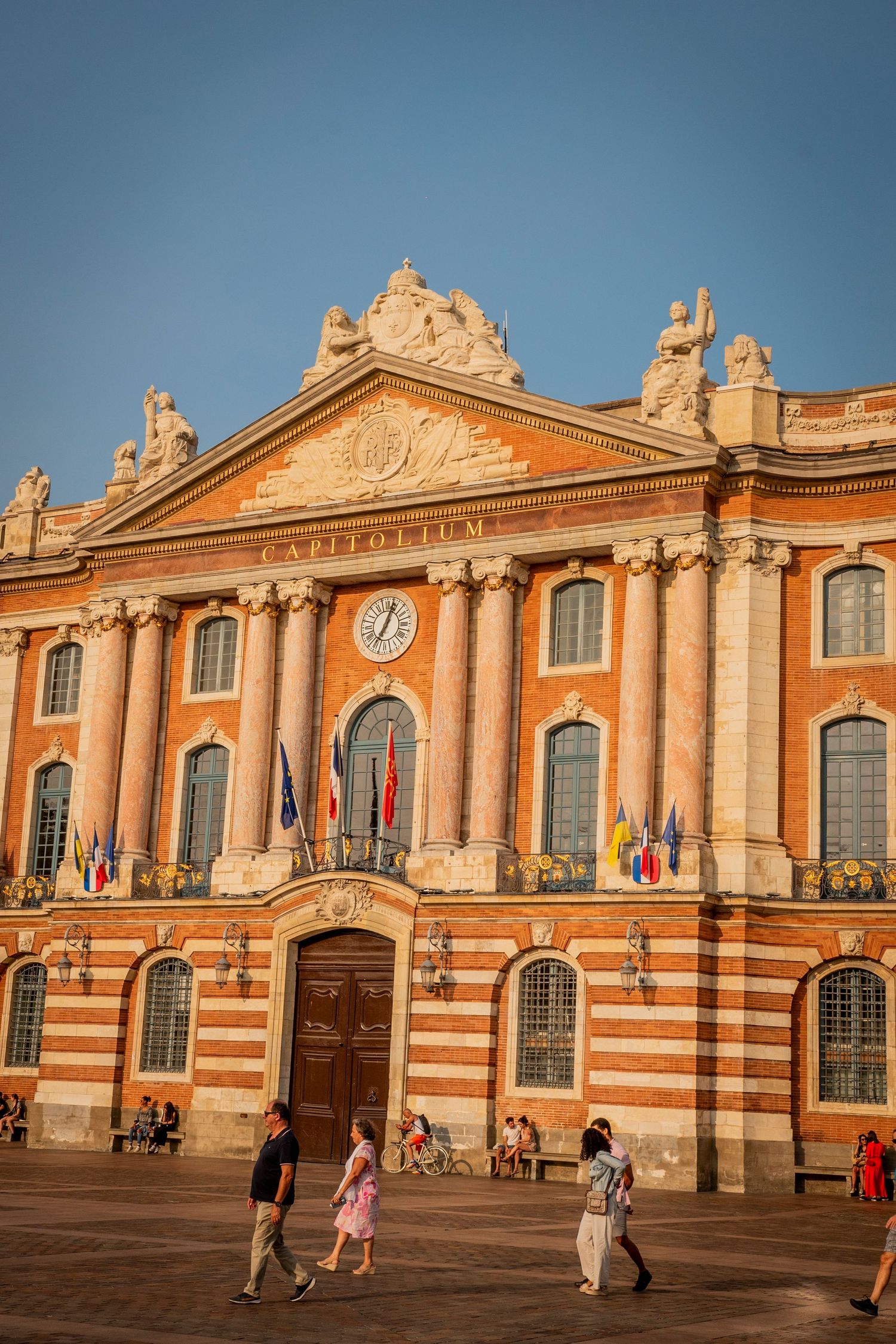 Historic orange and white Toulouse train station building with ornate architectural details glows in warm sunset light.