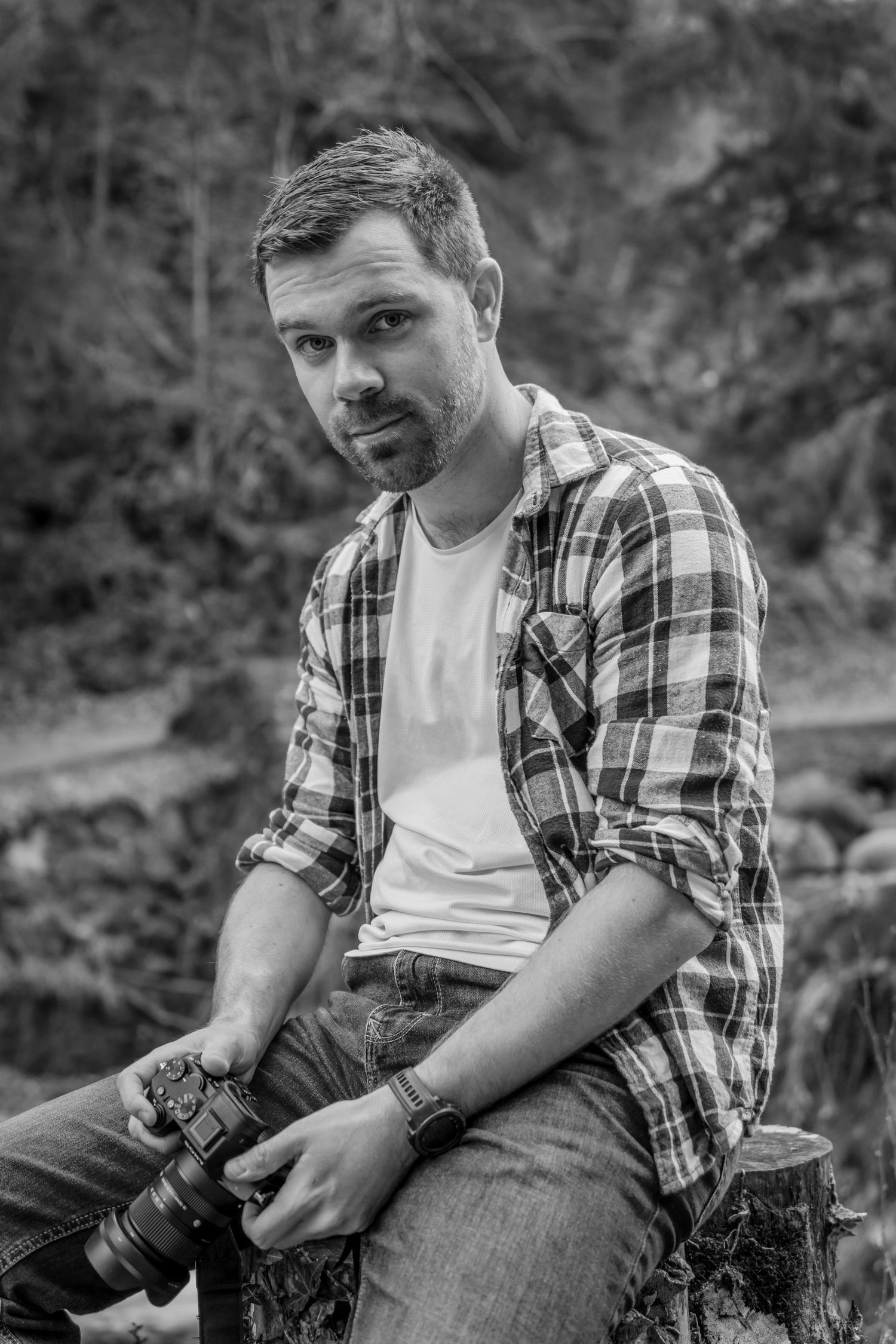 Professional photographer in plaid shirt holding DSLR camera in outdoor nature setting.
