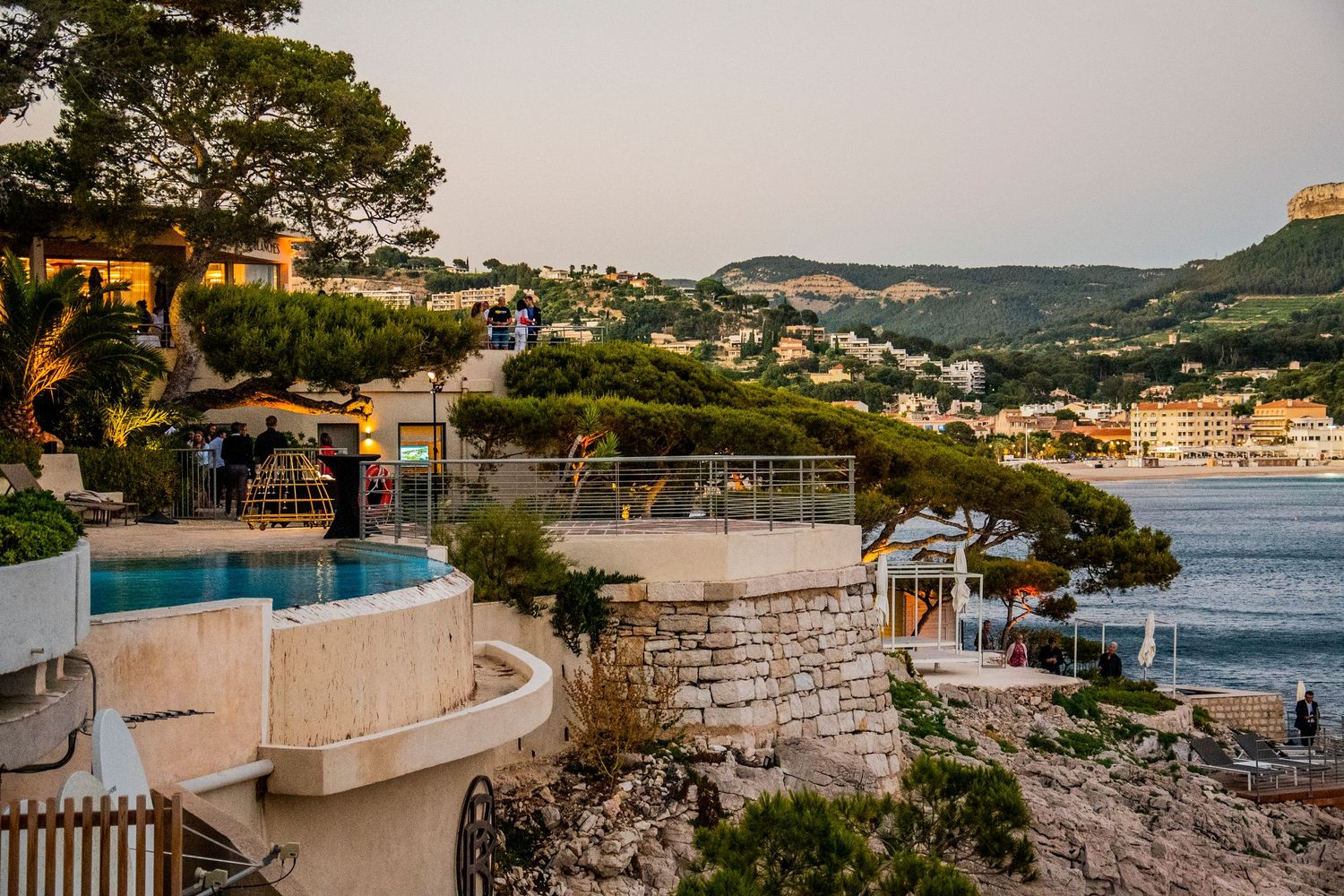 Mediterranean coastal scenes show waterfront villas with swimming pools overlooking a scenic bay at sunset.