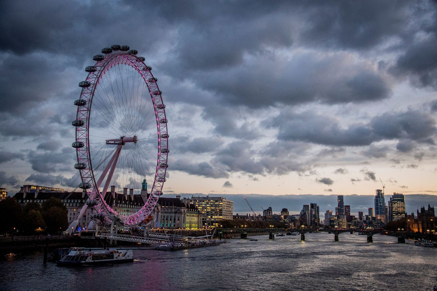 London Eye and Thames River at sunset with dramatic storm clouds looming over the cityscape.