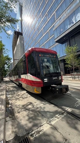 A modern red and white streetcar or light rail vehicle stopped in front of a glass office building on a sunny day.