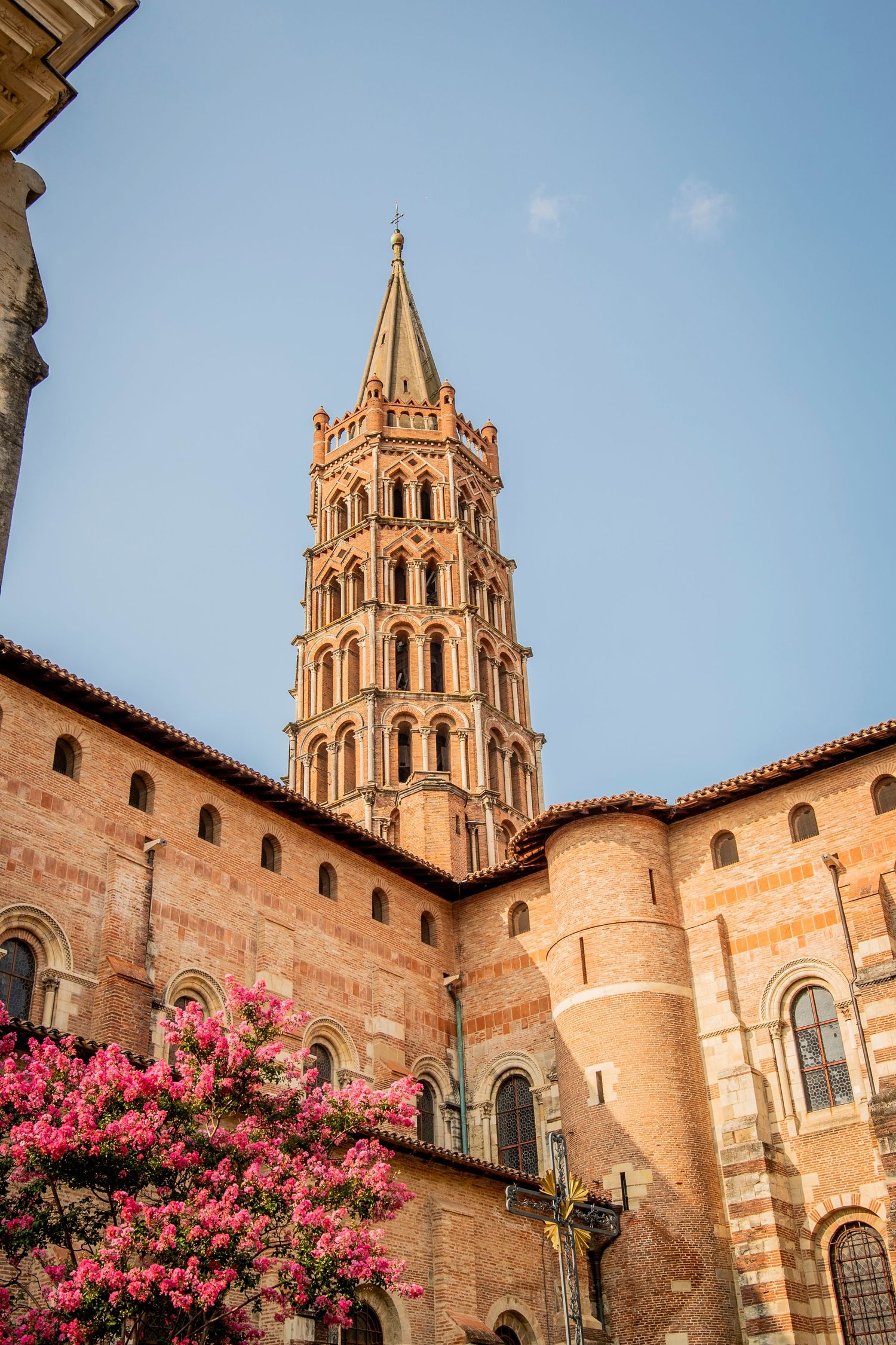 Gothic bell tower of Saint-Sernin Basilica in Toulouse with pink blossoms in foreground against blue sky.