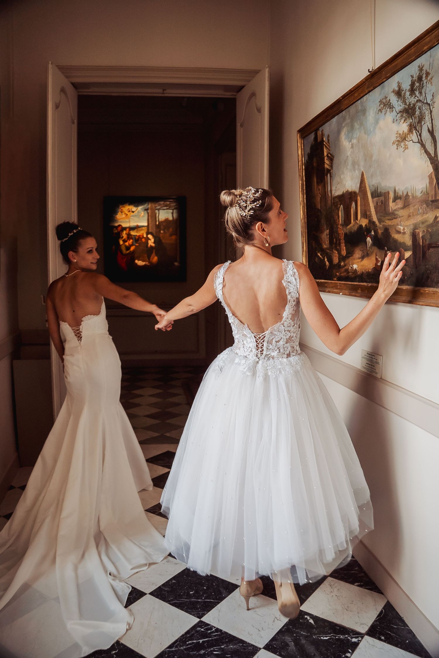 Two wedding gowns in bright white and cream colors displayed in an elegant hallway with art adorning the walls.