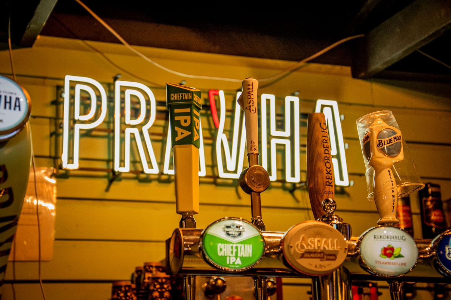 Illuminated neon 'PRIV HY' sign mounted above beer taps in a dimly lit bar setting.