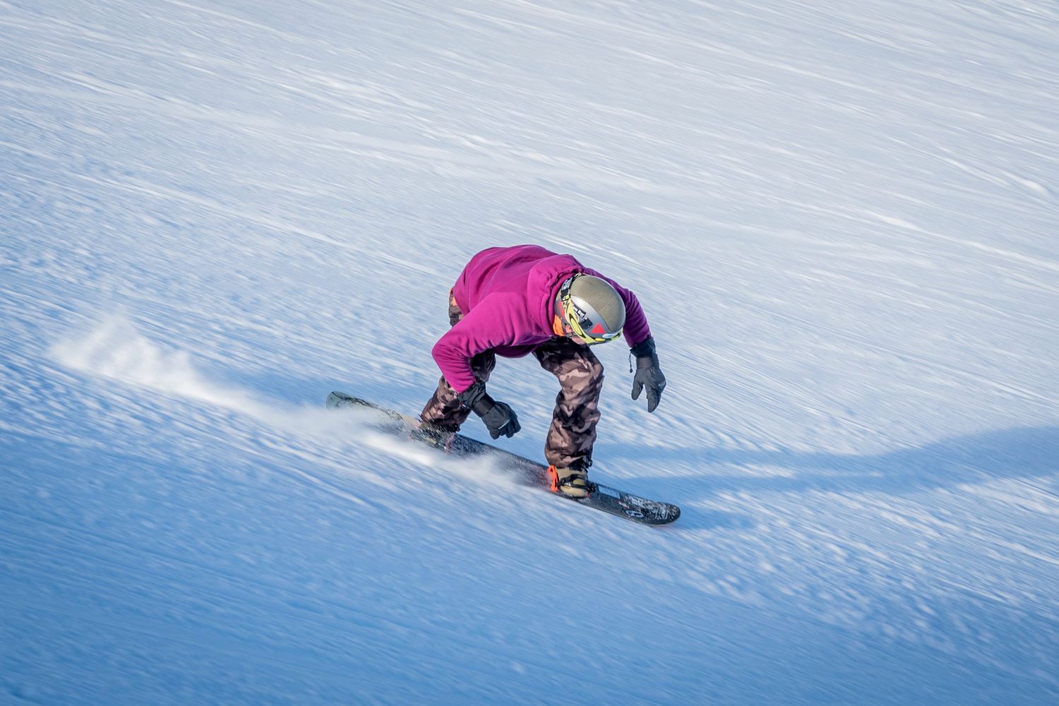 Snowboarder in pink jacket performs backside turn on snowy slope with dynamic low angle perspective.