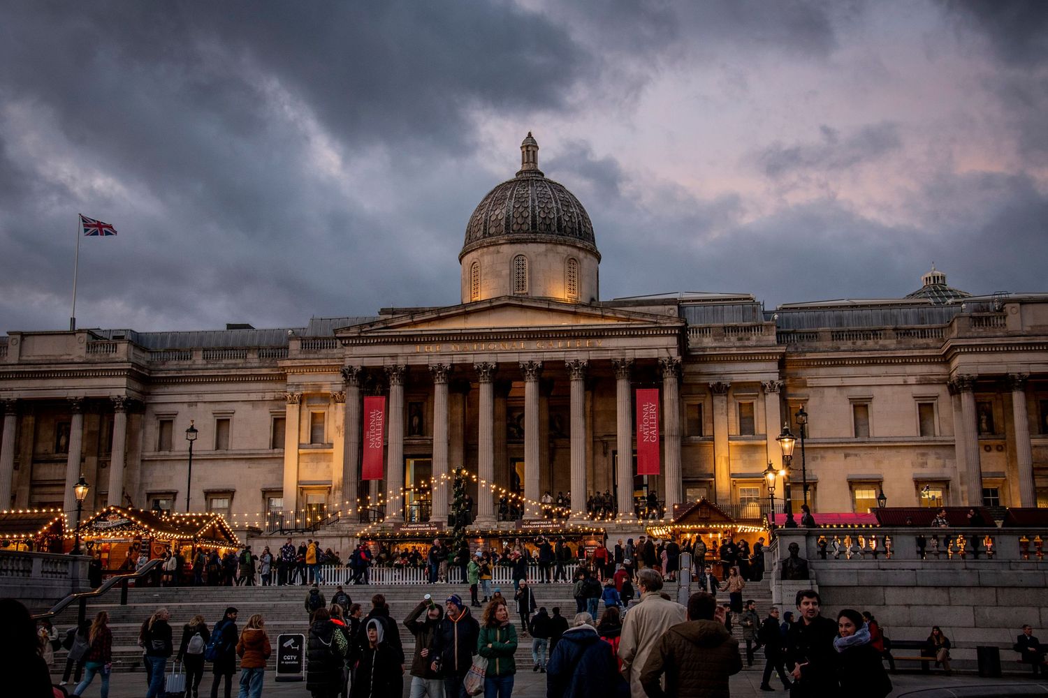 Crowds gather at dusk outside the National Gallery in London's Trafalgar Square as storm clouds loom overhead.