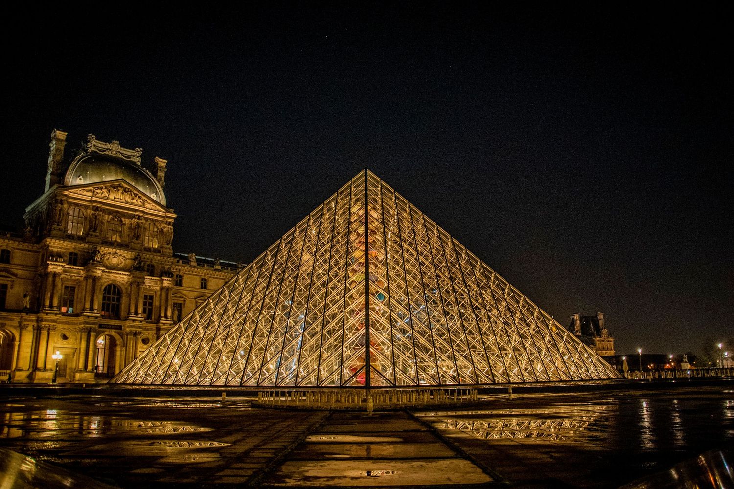 Illuminated glass pyramid entrance of the Louvre Museum in Paris glows against the historic palace at night.