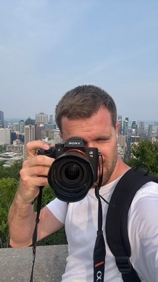 A photographer takes a photo with a Sony camera against a Montreal cityscape backdrop on a sunny day.