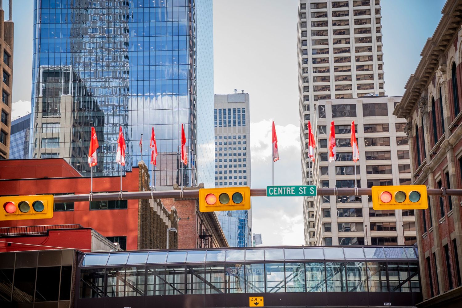 Modern glass skyscrapers and vibrant red flags line a busy downtown intersection with traffic lights in a thriving city.