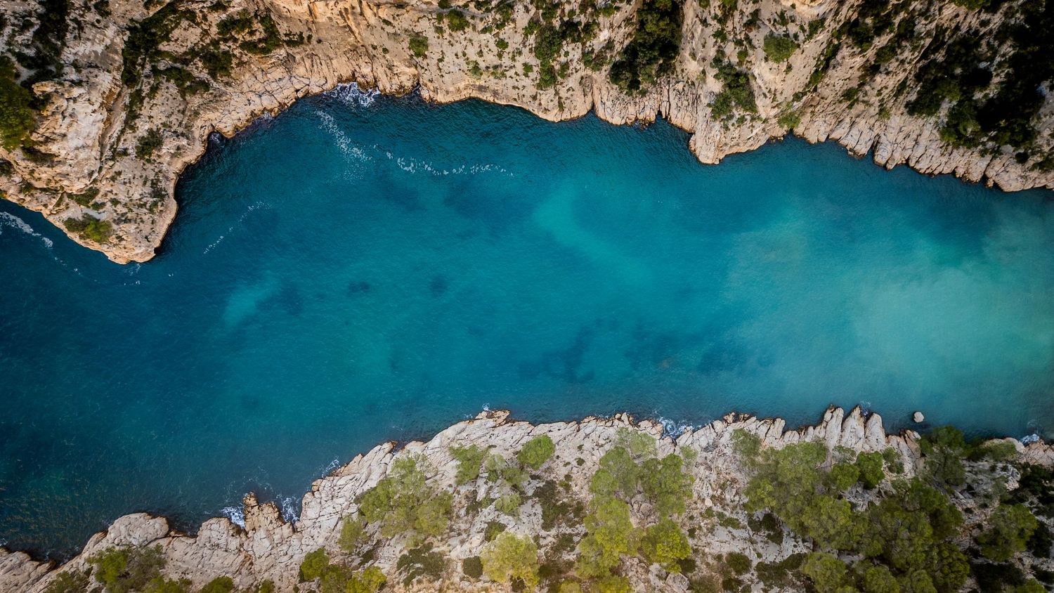 Aerial panoramic view of rugged coastal cliffs meeting crystal blue Mediterranean waters.