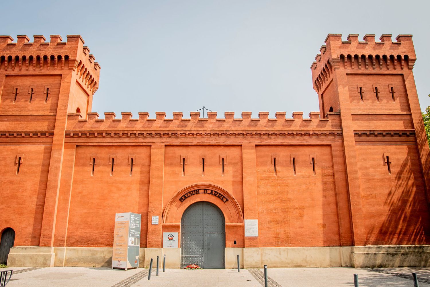 Ancient red fortress walls and towers with ornate crenellations stand against a bright blue sky in India.