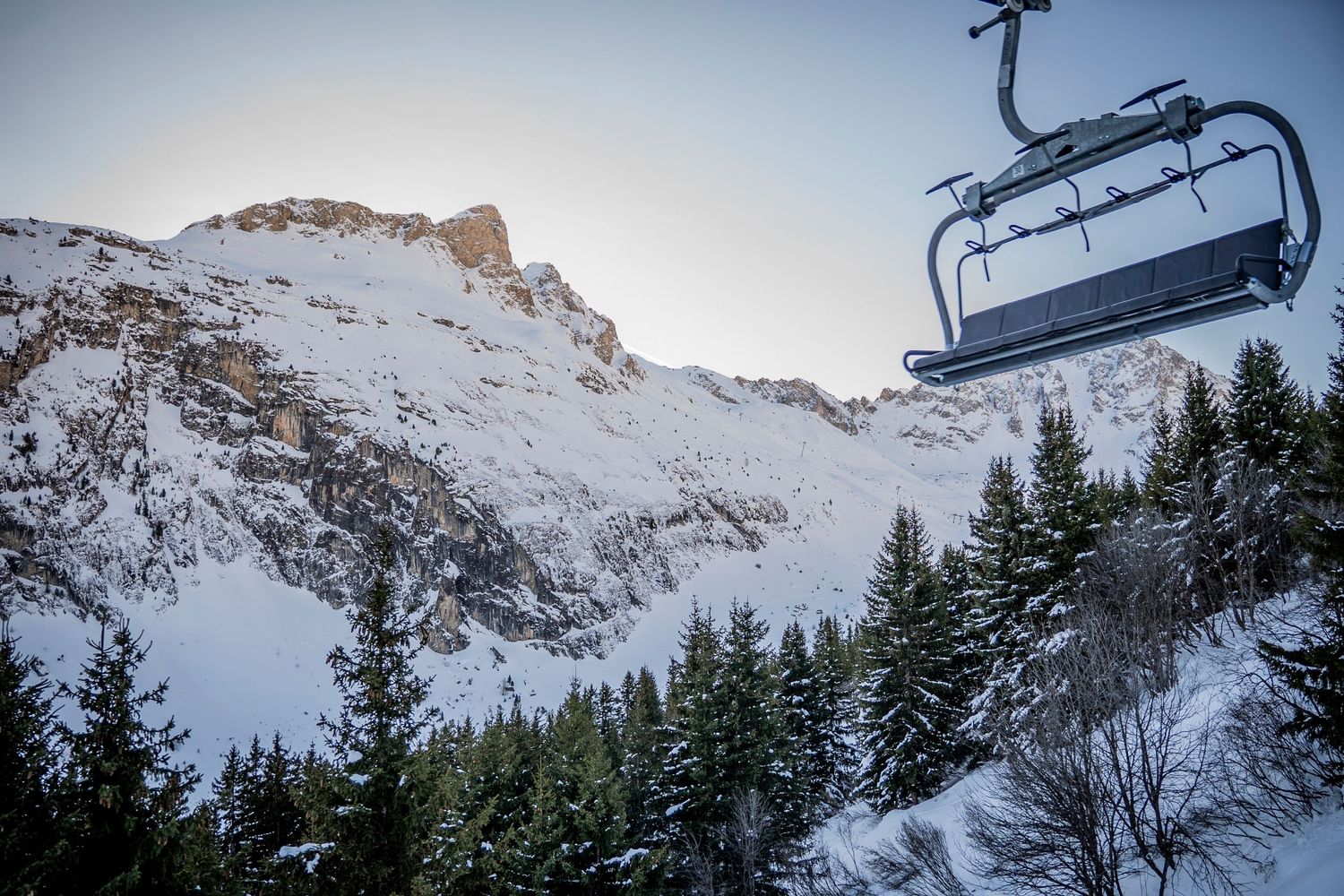 Snowy mountain peaks and ski lifts soar above evergreen forests in a scenic winter landscape at dusk.
