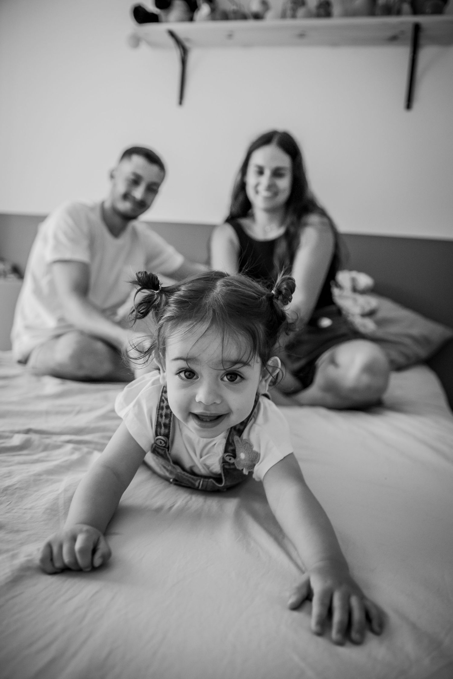 A child crawls and plays while having fun on a plush white bed during a candid black and white photoshoot.